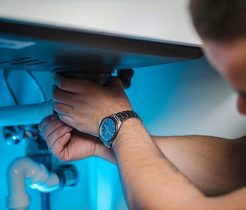 A plumber works under a sink to inspect and repair the plumbing system